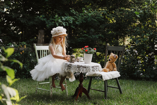 A beautiful little girl, four years old, having a tea party with her teddy bear in the garden.