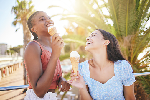 Ice cream, summer and women friends eating on Miami beach for holiday travel, vacation and outdoor youth lifestyle with sunshine lens flare. Happy, diversity teenager couple with icecream dessert