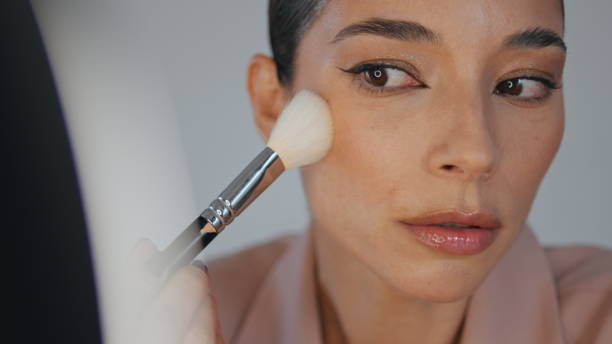 istock Closeup lady powdering face using brush home. Woman applying foundation makeup 1799490380