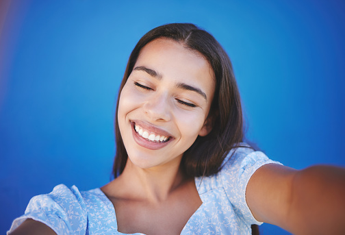 Happy woman with natural beauty, taking selfie for social media and with smile on face against blue background. Portrait of pretty young girl, body wellness and glowing healthy skin on summer holiday
