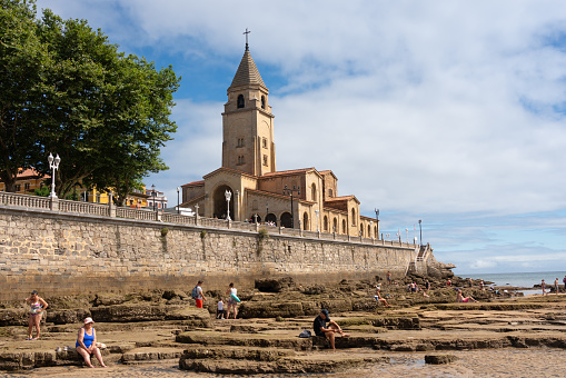 People enjoying the summer on San Lorenzo beach next to the church of San Pedro in the city of Gijón. Asturias. Spain. August 1, 2023.