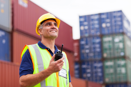 smiling middle aged warehouse worker holding radio at container yard