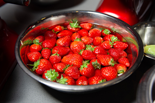 Vibrant strawberries, meticulously soaked in water, presented in a steel bowl. A refreshing image capturing the essence of freshness of the ripe berries