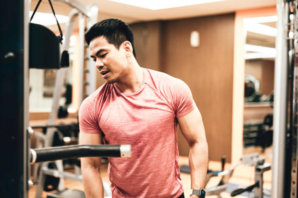 joven que se ejercita en la máquina de remo en el gimnasio - body care asian ethnicity body building toughness fotografías e imágenes de stock