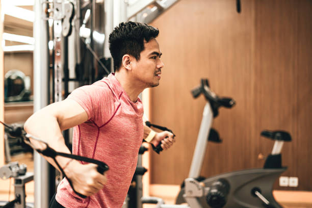 joven que se ejercita en la máquina de remo en el gimnasio - body care asian ethnicity body building toughness fotografías e imágenes de stock