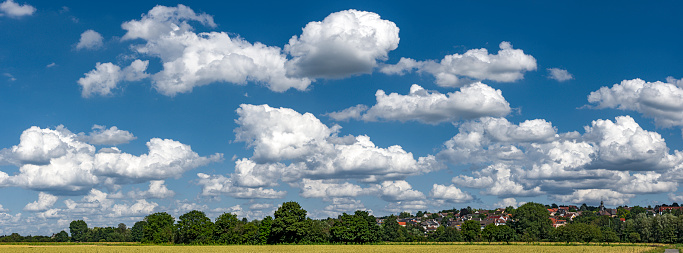 Panoramic view of the blue sky slightly overcast with cumulus clouds, cumulus clouds or fair weather clouds and fleecy clouds above the horizon with houses, fields and woodlan