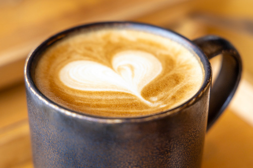 Heart coffee. Roasted coffee beans in the shape of heart on bright stone background. Concept of coffee love, Valentines Day, good mood, gift. With wooden spoon.