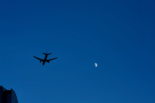 A large passenger plane, approaching Haneda Airport in a landing position, flies over the moon and high-rise office buildings as it heads towards the central part of Tokyo.