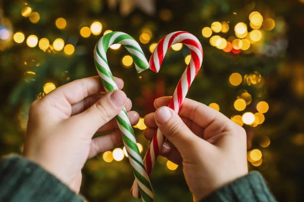 istock Child's hands with candy canes in heart shape over Christmas tree background 1799818777