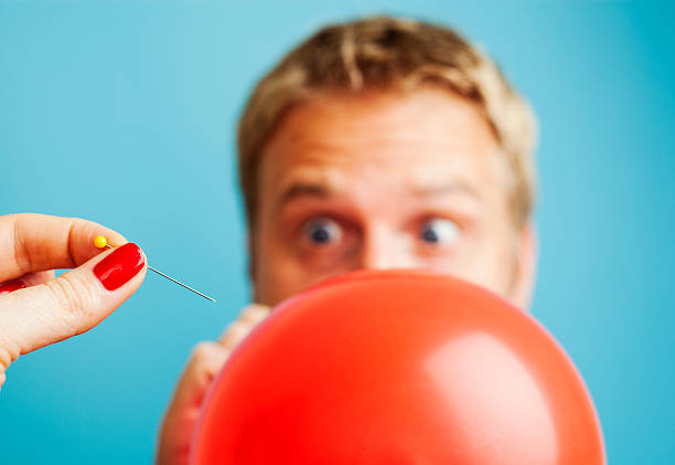 Blonde man blowing up a balloon about to be popped stock photo