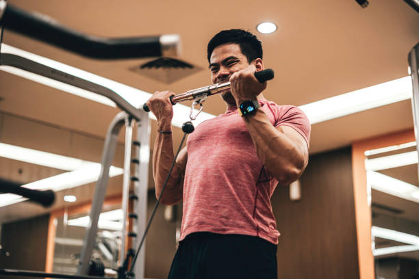 joven que se ejercita en la máquina de remo en el gimnasio - body care asian ethnicity body building toughness fotografías e imágenes de stock