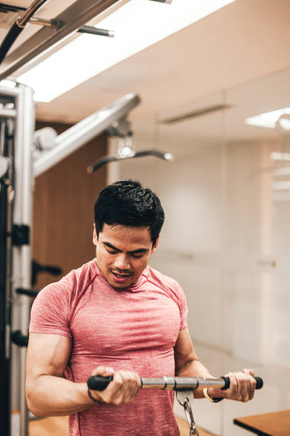 joven que se ejercita en la máquina de remo en el gimnasio - body care asian ethnicity body building toughness fotografías e imágenes de stock