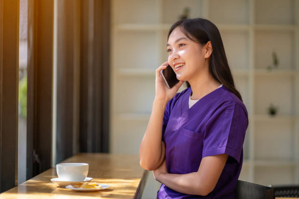 medico femminile rilassato che beve caffè chatta con gli amici sul tuo cellulare e mangia spuntini durante le pause. - clothing protective workwear authority anticipation foto e immagini stock