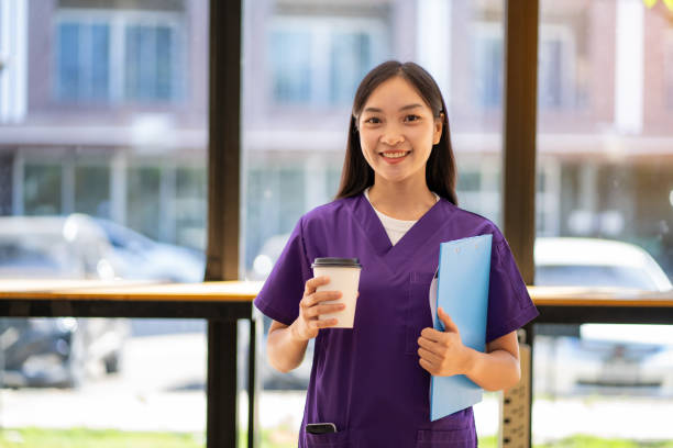 medico femminile che tiene una tazza di caffè e abbraccia i file durante le pause pranzo - clothing protective workwear authority anticipation foto e immagini stock