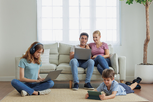 A modern Caucasian family engages with various gadgets at home, blending technology seamlessly into their daily lives and interactions