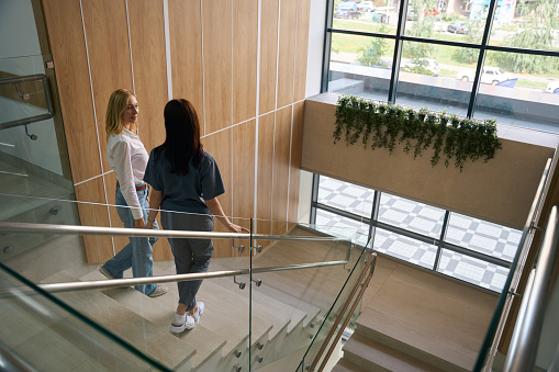 Mature woman talking to female doctor while walking down stairs in medical facility