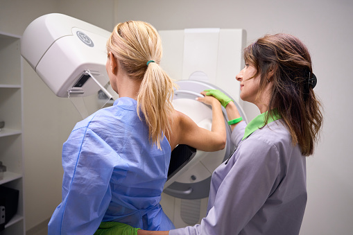 Mammographer resting the patient arm with elbow bent across top of receptor on mammography unit