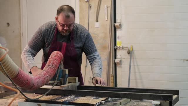 Carpenter feeds wood through a table saw, hands guiding with expertise. The scene underscores the importance of skilled labor in a machine-driven age