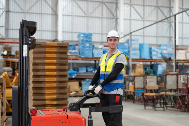 Man worker driver using forklift electric or electric pallet stacker lift moving cardboard boxes sheet goods in paper box factory. Male warehouse worker working in store warehouse. conductor de trabajador que usa carretilla elevadora eléctrica o apiladora de paletas eléctrica que mueve cajas de cartón en productos de hoja en fábrica de cajas de papel. trabajador de almacén masculino que trabaja en el almacén de la tienda.