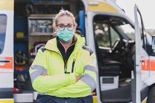 Young female paramedic waiting for emergency call in front of an ambulance