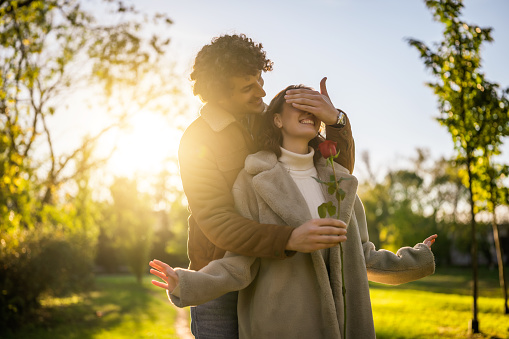 Portrait of happy loving couple in park in sunset. Man is giving rose to his woman.