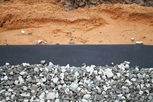 Geotextile with gray gravel above sandy backdrop