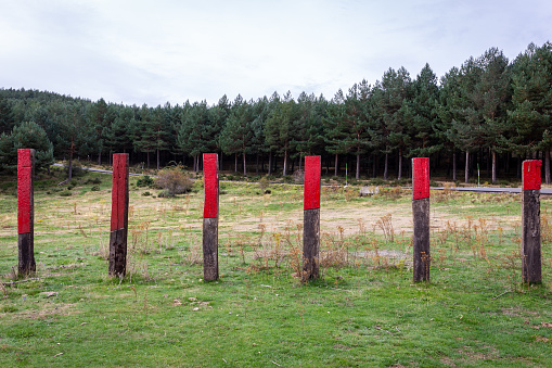 Wooden fence piles with red markings against cattle at Aparcamiento Morcuera II capming site on M-611 road in Sierra de Guadarrama mountains, Spain, pine forest in the background.