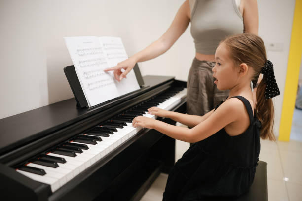 Young pianist teacher teaching girl kid student to play piano, music education concept Mother teaching daughter to play piano. The girl is aged 6. Mother and girls are sitting by the old piano in a sunny room. girl playing piano stock pictures, royalty-free photos & images