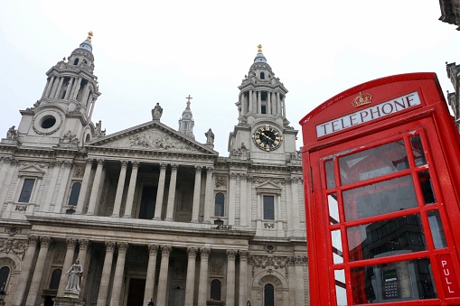 A blonde tourist woman stands in a classic, red telephone booth in front of the Big Ben clocktower in London during a sightseeing trip