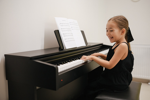 Little girl playing piano,facing camera and smiling. She's about 6 years old of which two years in piano lessons.