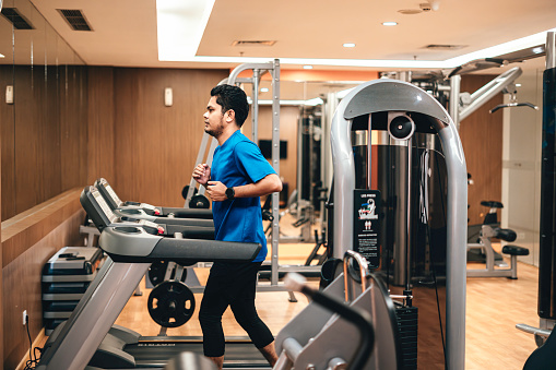 Young determined man running on treadmill during sports training in a gym.