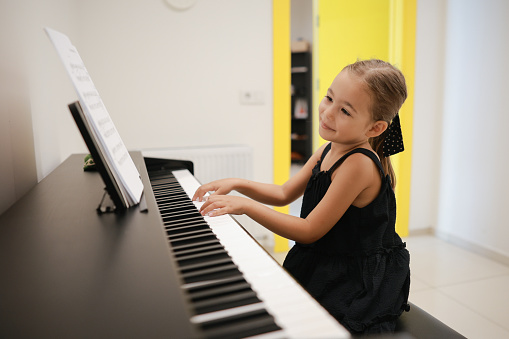 Portrait of adorable young asian kid practicing the piano alone at home