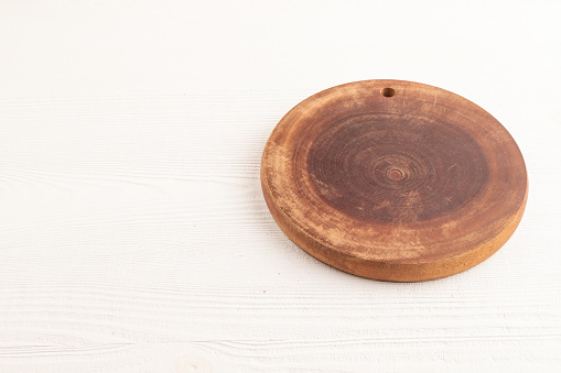 Empty round wooden cutting board on white wooden background. Side view, copy space.