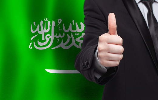 Saudi Arabian concept. Businessman showing thumb up on the background of flag of Saudi Arabia