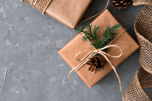 Aesthetic Christmas presents on gray table background. Brown gift boxes decorated with crafter paper, conifer twigs and pines. Sustainable ecological winter holiday celebration concept.