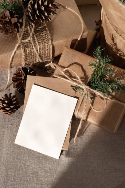 istock Crafted brown gift boxes and blank paper card mockup , envelope on beige table background in sunlight with shadow. Rustic Christmas presents and greeting postcard, branding template, lifestyle 1800317717