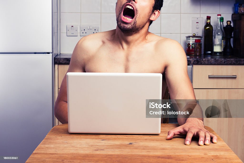 A naked man watching pornography in his kitchen A naked man is watching pornography on a laptop in his kitchen and masturbating Pornography Stock Photo