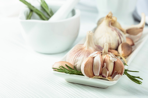 Fresh garlic bulbs with rosemary on a white kitchen table.
