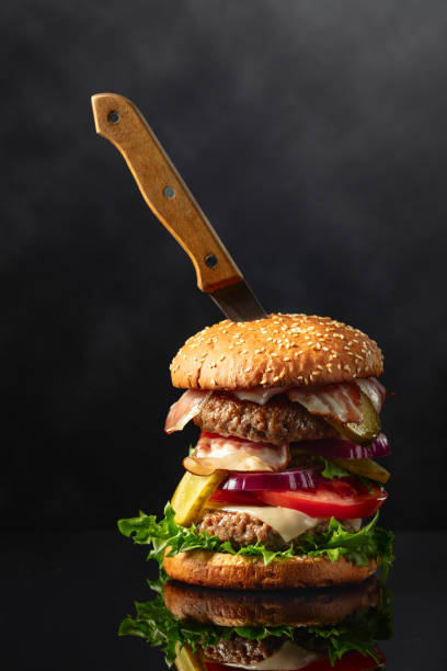 istock Fresh tasty burger with knife on a black reflective background. 1800342637