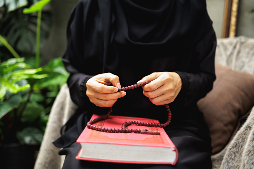 A close-up shot captures the hands of a person in religious attire, intricately handling prayer beads over an open holy book, reflecting deep spiritual engagement