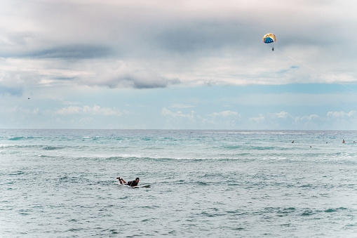 A wide view of an unrecognizable man laying on his surfboard and paddling while waiting for the perfect wave off the coast of Hawaii.