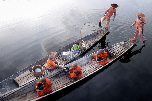 Inle Lake,Shan State,Myanmar-August 14 2023 : At the Inle Lake fisherman family on their boat and  a fisherman is standing on one leg at the stern while his wife to offer foods to monks in the morning.This is a routine of Buddhists at the Inle Lake they are often make a merit and offering to monks in everyday mornings.