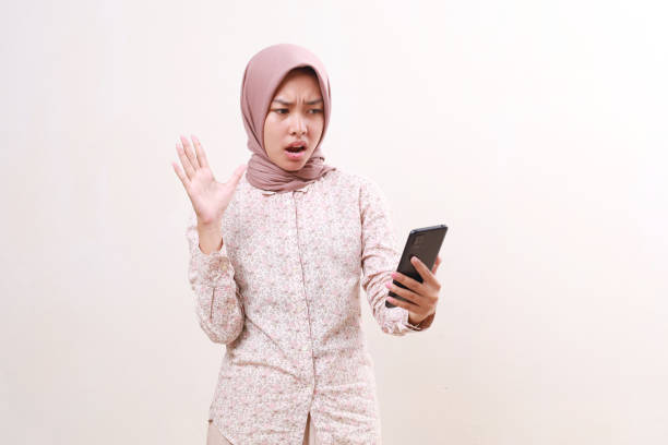 istock Shocked young asian muslim girl standing while getting message from her cell phone. Isolated on white 1800435772