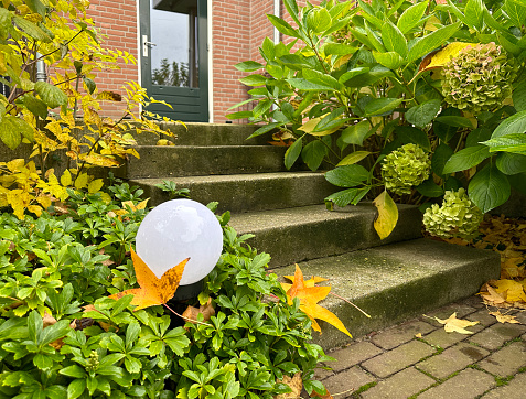 Autumn leaves lie around the doorstep. Solar lamp powered by a solar energy. This is perfect solution to care for the environment