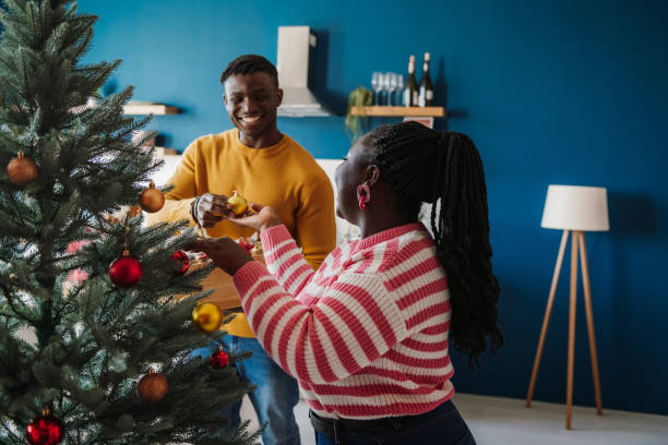 istock Joyful young African couple enjoying fun time while decorating Christmas tree at home together 1800439378