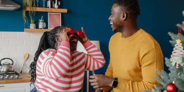 Happy young African couple having fun while decorating Christmas tree at home together