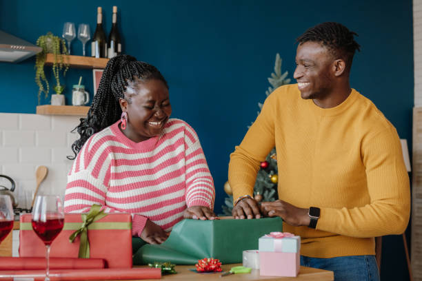 Beautiful young African couple looking joyful while wrapping Christmas gifts in at home together