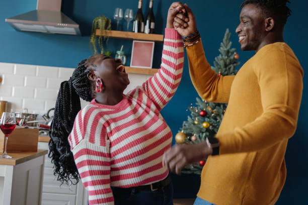 Beautiful young African couple dancing and smiling while celebrating Christmas holiday at home together