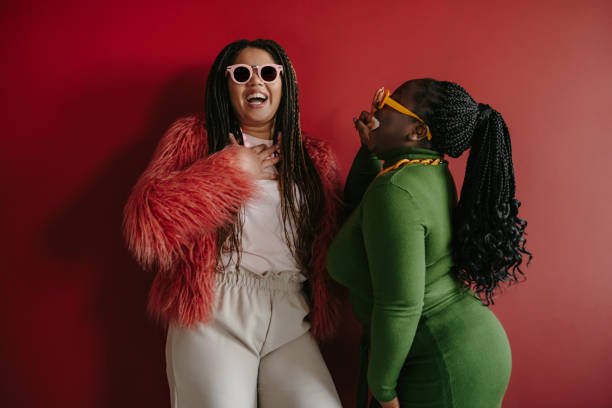 istock Two joyful plus size African woman with braided hair having fun while standing on red background together 1800439601