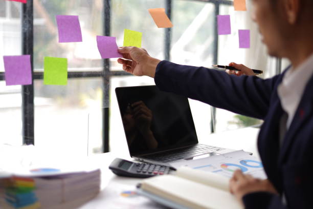 istock Businessmen and colleagues brainstorming scheduling business strategy, planning work in the office with paper stickers on the glass. 1800445009